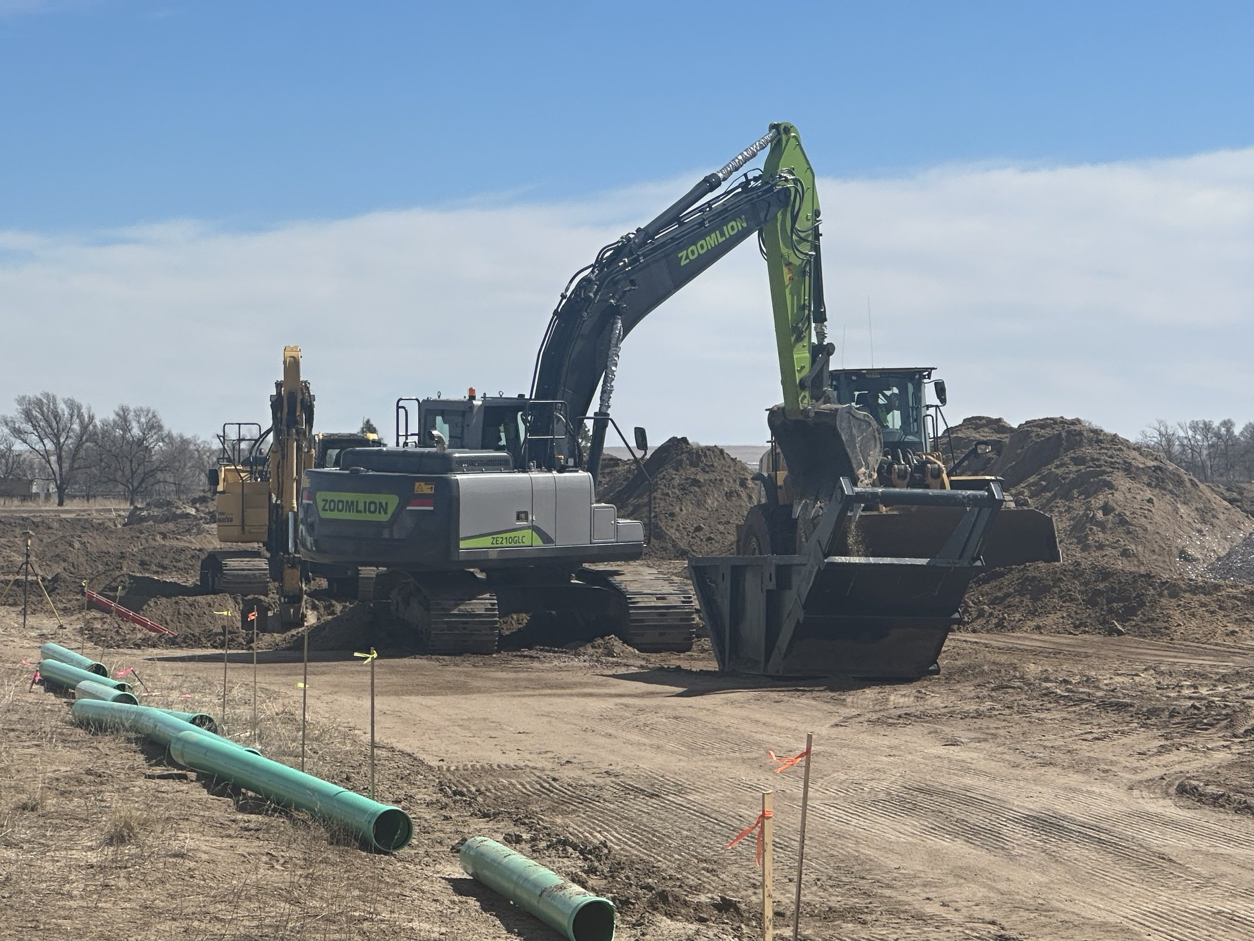 Three machines working on a construction pad: a Zoomlion excavator, a Komatsu excavator and a Cat wheel loader.